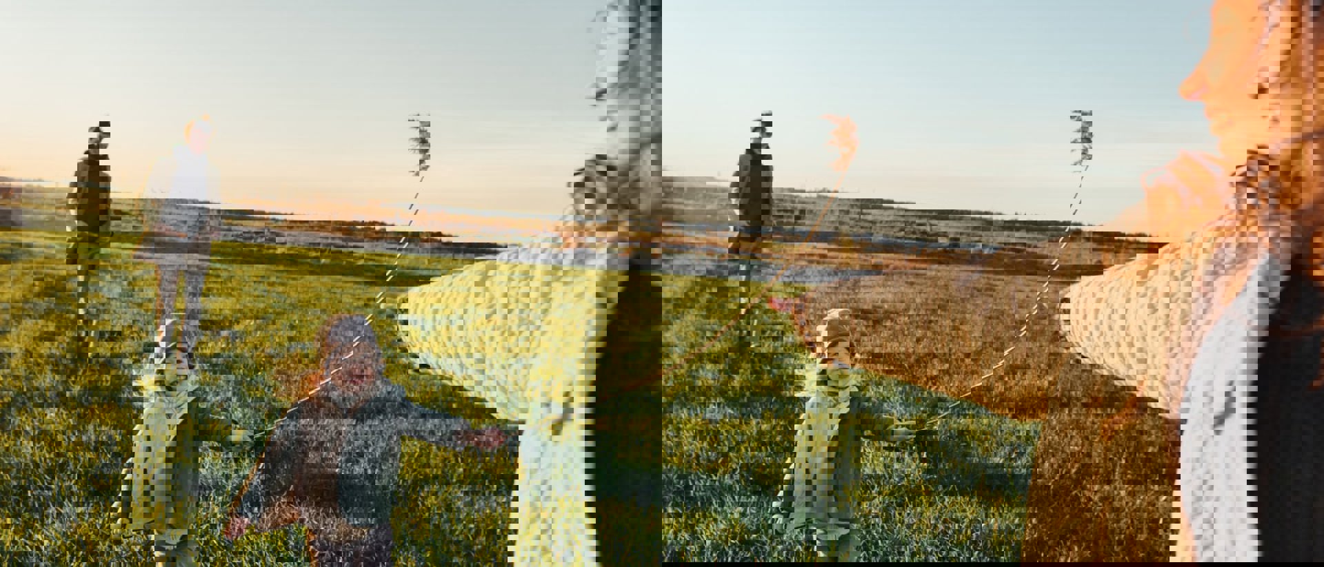 family bundled up in jackets and scarves fly a kite in a field at sunset